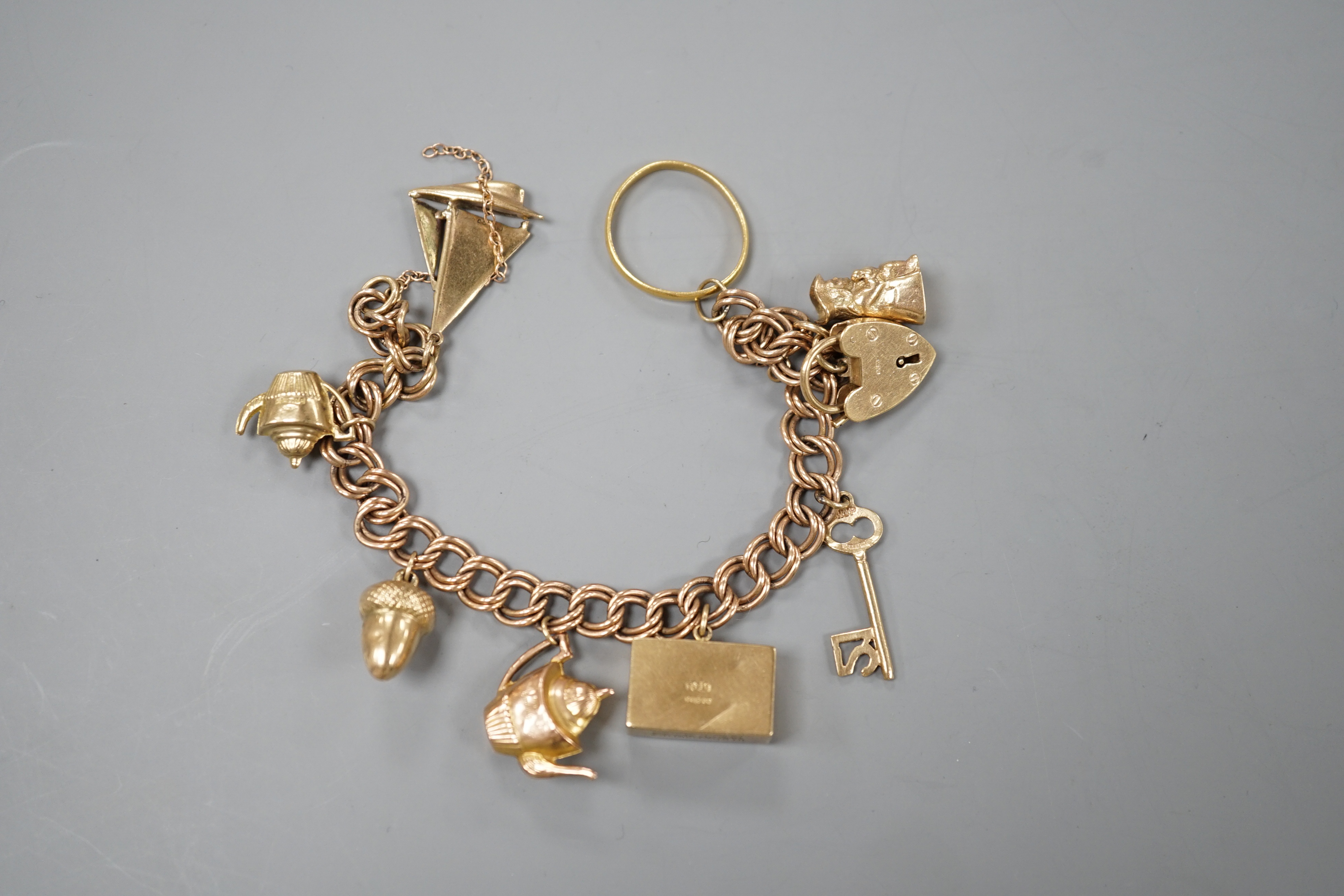 A 1960's 9ct gold charm bracelet, hung with eight assorted mainly 9ct gold charms and a 22ct gold wedding band, gross 28.4 grams.